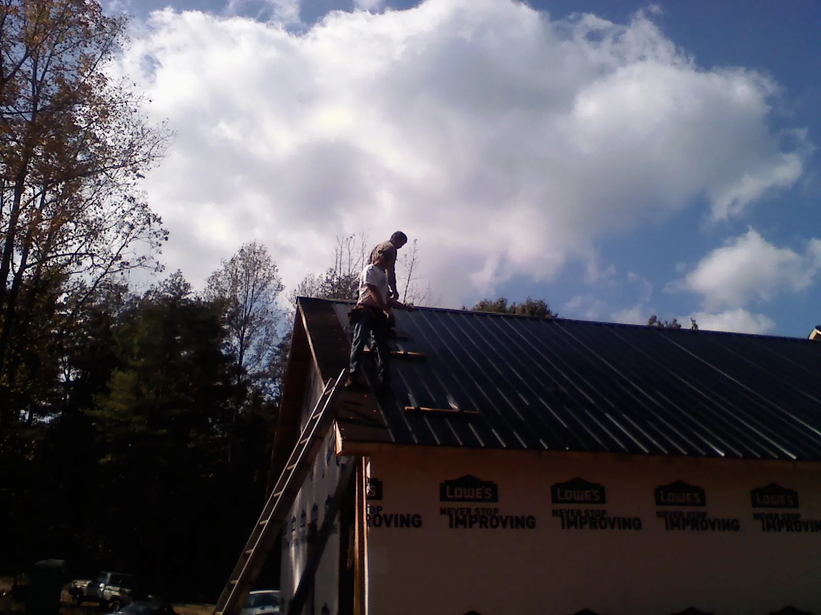 Roofer fastening dark metal panels high against a cloudy sky, from a Roof Inspection job in Clayton